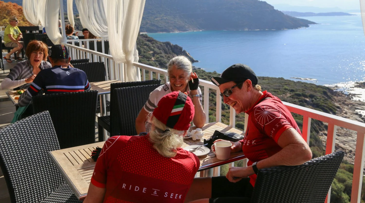 Cyclists enjoying refreshments at seaside terrace cafe during Ride & Seek bicycle tour with ocean views