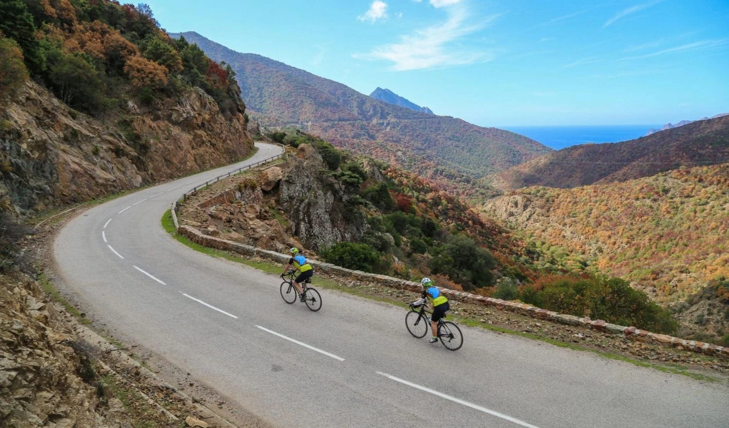 Cyclists ascending winding mountain road with colorful autumn foliage on Ride & Seek Alpine tour