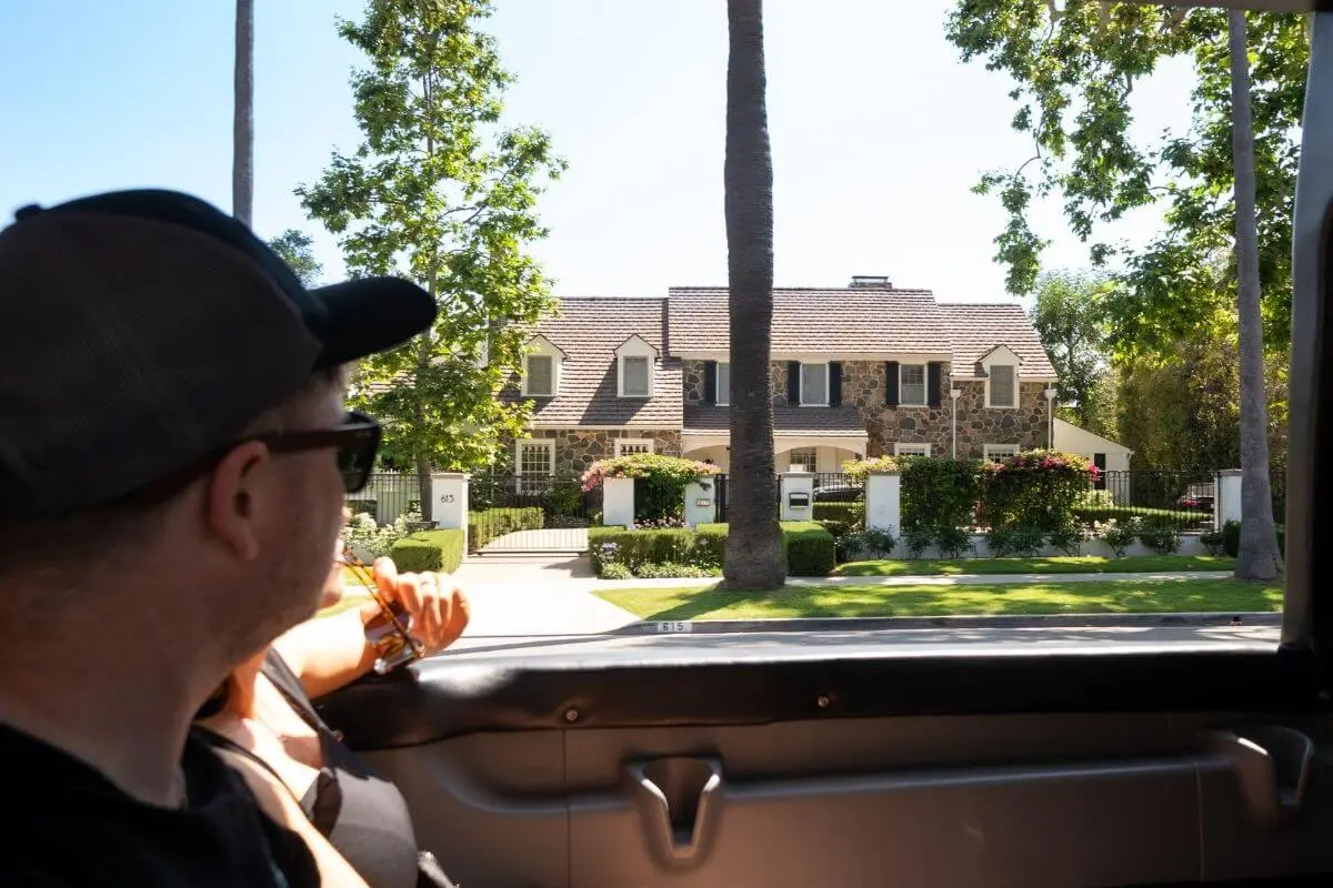 Tour guests looking out from an open-top Hollywood Bus Tour at a beautiful Beverly Hills mansion during a celebrity homes tour in Los Angeles