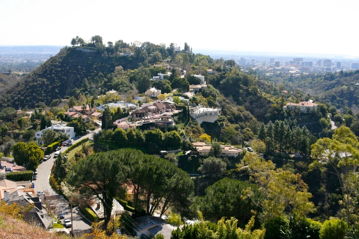Exclusive hilltop celebrity mansions and estates perched on prominent Hollywood Hills peak with Los Angeles cityscape visible in background, showcasing luxury architecture and extensive properties accessible via sightseeing tours.
