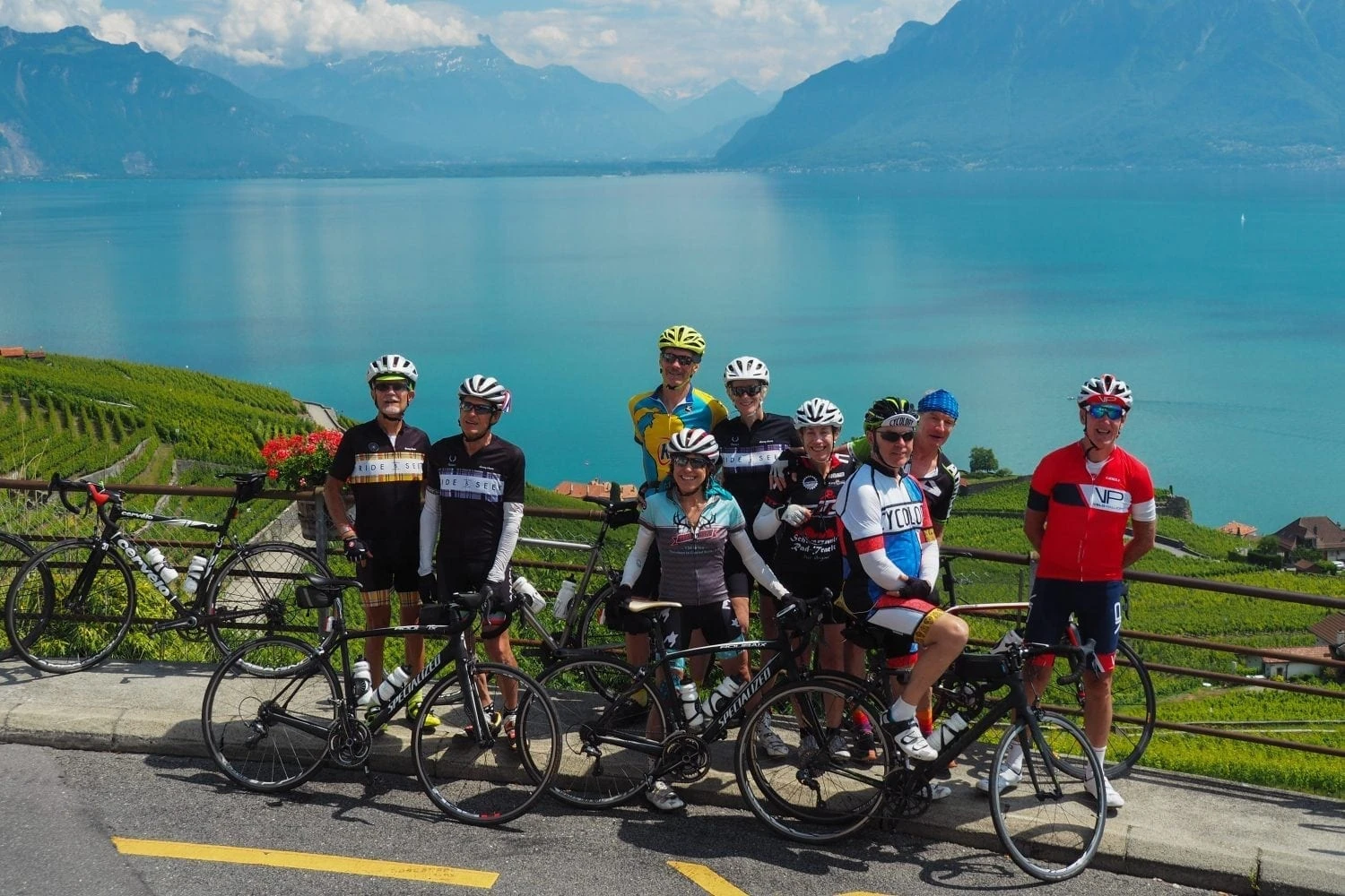 Ride & Seek cycling group posing with bikes overlooking Lake Geneva and Swiss Alps mountains