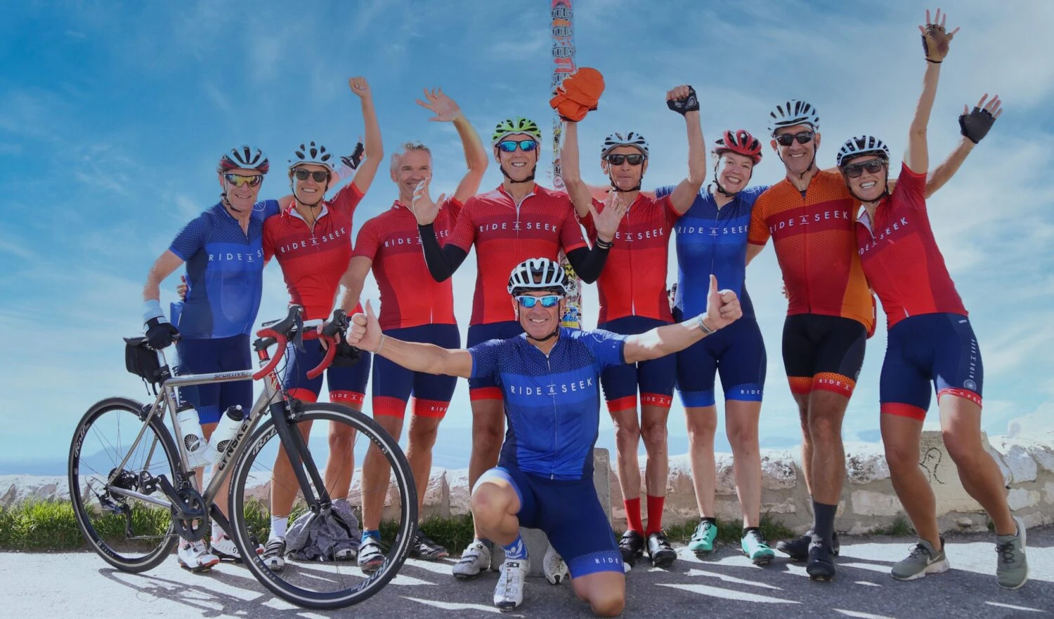 Happy Ride & Seek cycling group celebrating at mountain summit wearing branded jerseys and helmets