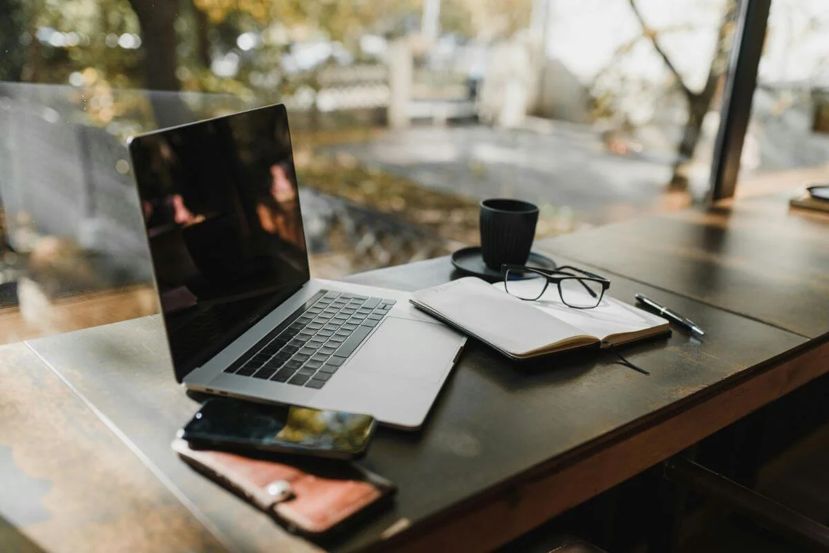 A laptop, notebook, glasses, and coffee on a desk by a window, representing a travel brand’s content and SEO planning for improving AI visibility and showing up in AI-powered search results.