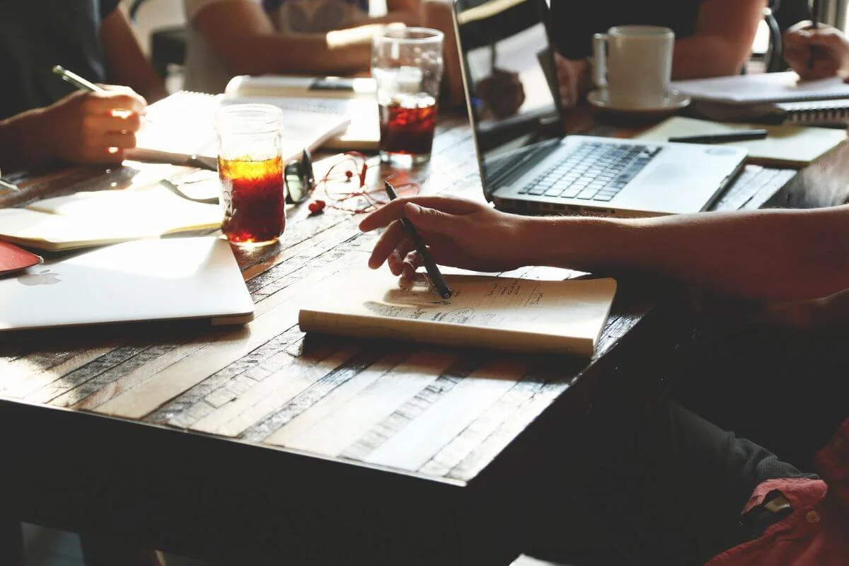 People collaborating at a table with laptops, notebooks, and drinks, representing planning and strategy for travel content and digital marketing.