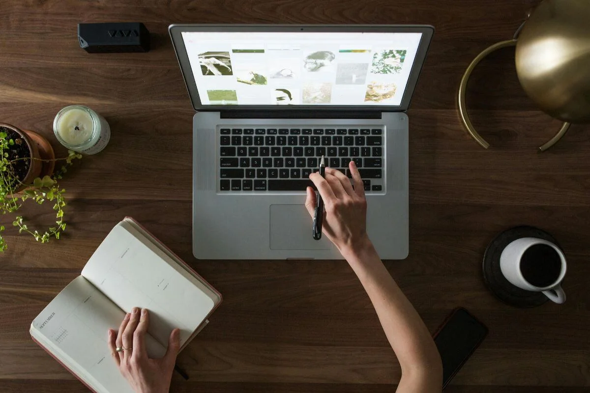Top-down view of a person working on a laptop at a wooden desk with a notebook, coffee, and desk accessories, representing content planning and digital strategy work.